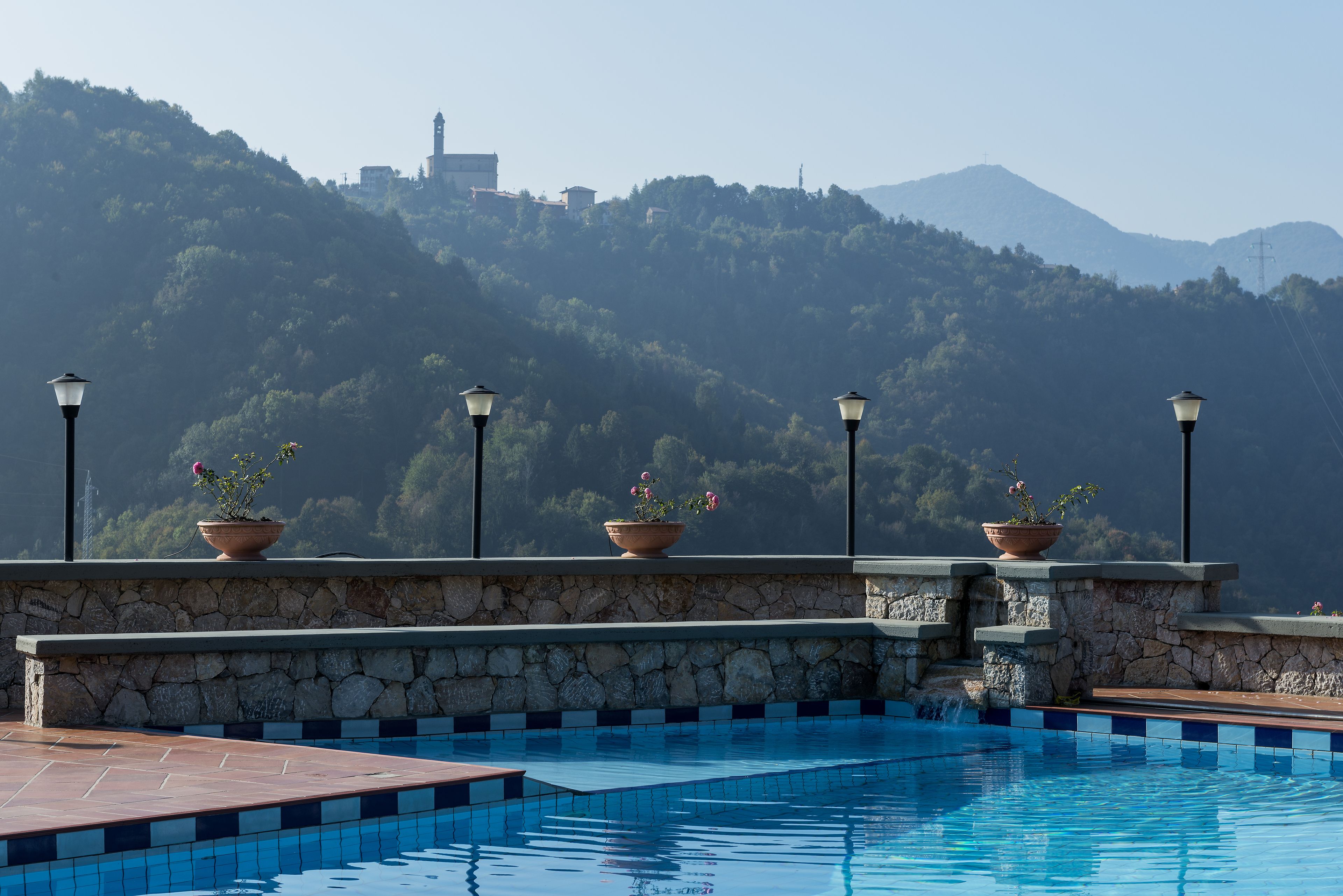 Ein Pool mit Steinstufen und Kübelpflanzen, umgeben von einer Steinmauer mit Blick auf eine gebirgige Landschaft.
