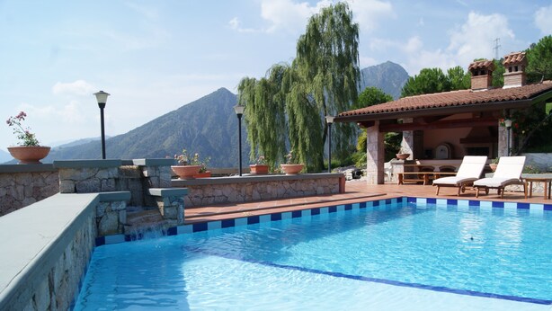 Una piscina con pared de piedra, plantas en macetas y vistas a montañas.