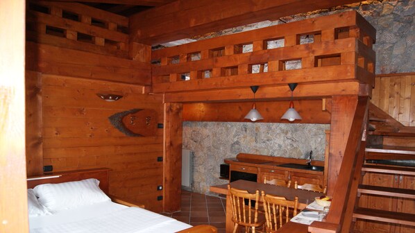 A wooden cabin interior with a bed, a dining table with chairs, and a kitchen area.
