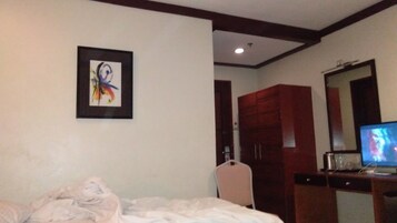 A hotel room with a bed, a television, a wardrobe, and a framed picture on the wall.