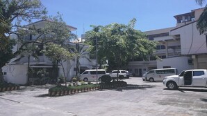 Un parking où sont stationnés plusieurs véhicules blancs, entouré de bâtiments et d’arbres.