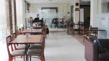 Un comedor moderno con mesas y sillas de madera, un piano y una persona sentada a una mesa al fondo.