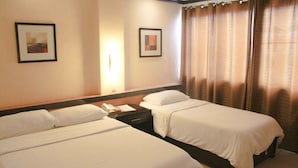 Une chambre d’hôtel avec deux lits, une table de chevet avec un téléphone et des documents, et une fenêtre avec des rideaux.