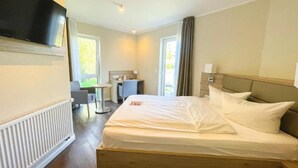 Una habitación de hotel con cama, televisión montada en la pared, escritorio y silla.