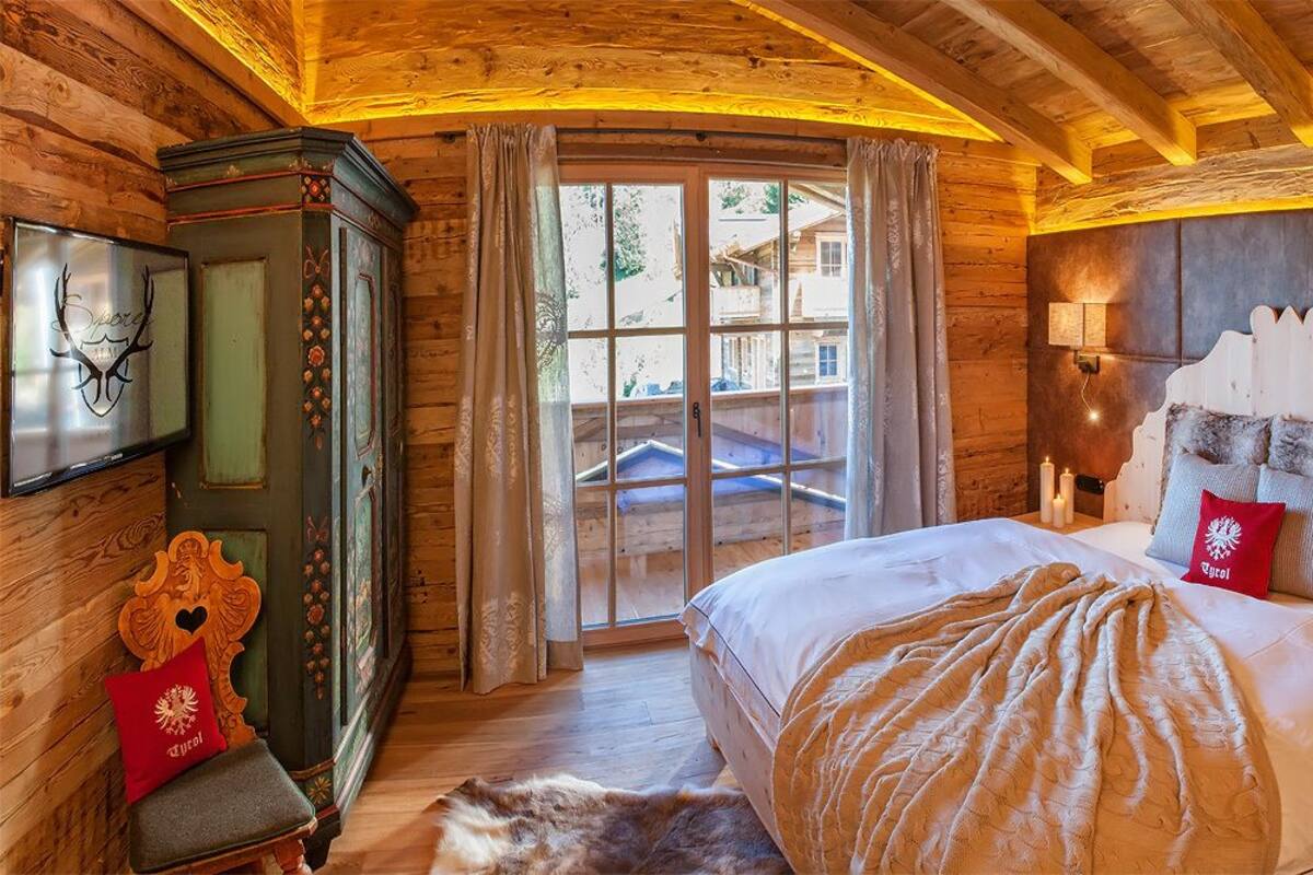 A cozy log cabin bedroom with a large bed, a wooden cabinet, and a view of the outside.
