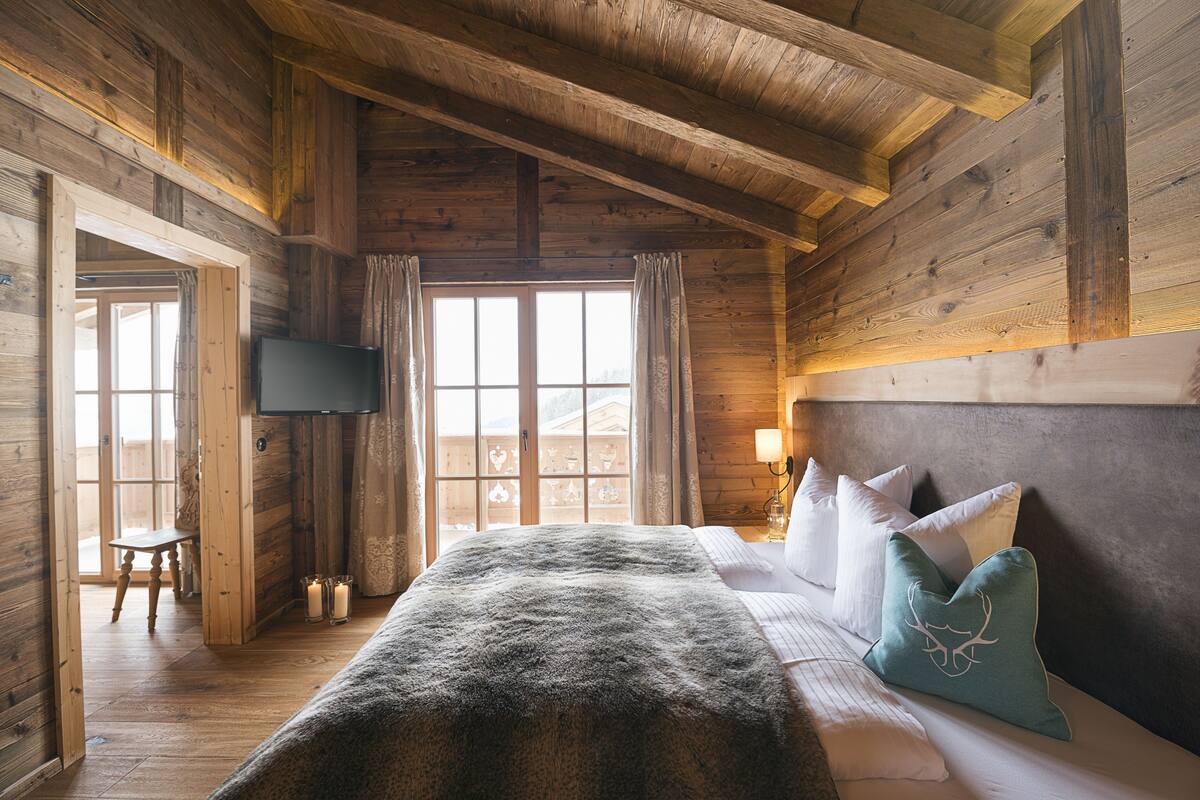 A wooden cabin bedroom with a bed, pillows, a TV, and a window.