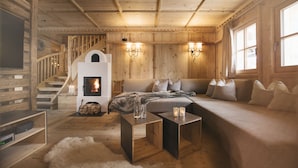 A cozy log cabin interior with a fireplace, wooden staircase, and a comfortable seating area.