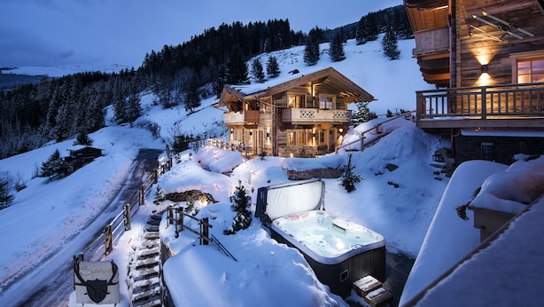 A log cabin with a hot tub and a ski lift in the background.