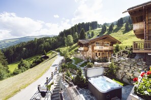A wooden chalet with a hot tub and stone walls, surrounded by a lush green landscape and a clear sky. - Sporer-Alm Alpine Residence (Rohrberg)