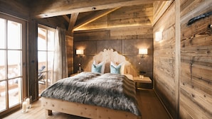 A wooden cabin bedroom with a bed, two bedside lamps, and a view through a large window.