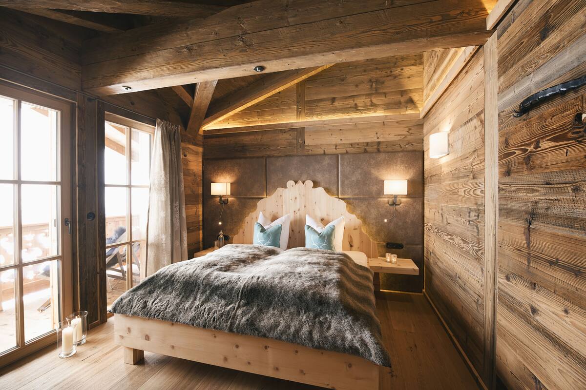 A wooden cabin bedroom with a bed, two bedside lamps, and a view through a large window.