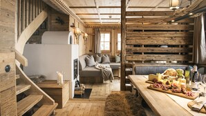 A rustic wooden interior with a staircase, a sofa, and a dining table set with food.