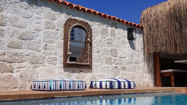A pool area with stone walls, a window, and striped cushions. - LilaVerde Alacati - Adults Only (Cesme)