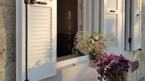 A house with white shutters, a wooden floor, and a white vase with flowers on the porch. - LilaVerde Alacati - Adults Only (Cesme)
