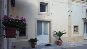 A building with a white door, a window, and a small balcony with potted plants. - Affittacamere Da Mary (Matera)