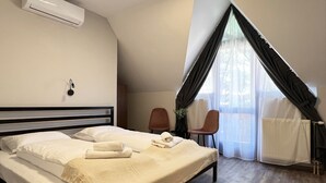 Un dormitorio con cama, ventana con cortinas, una silla y un equipo de aire acondicionado.