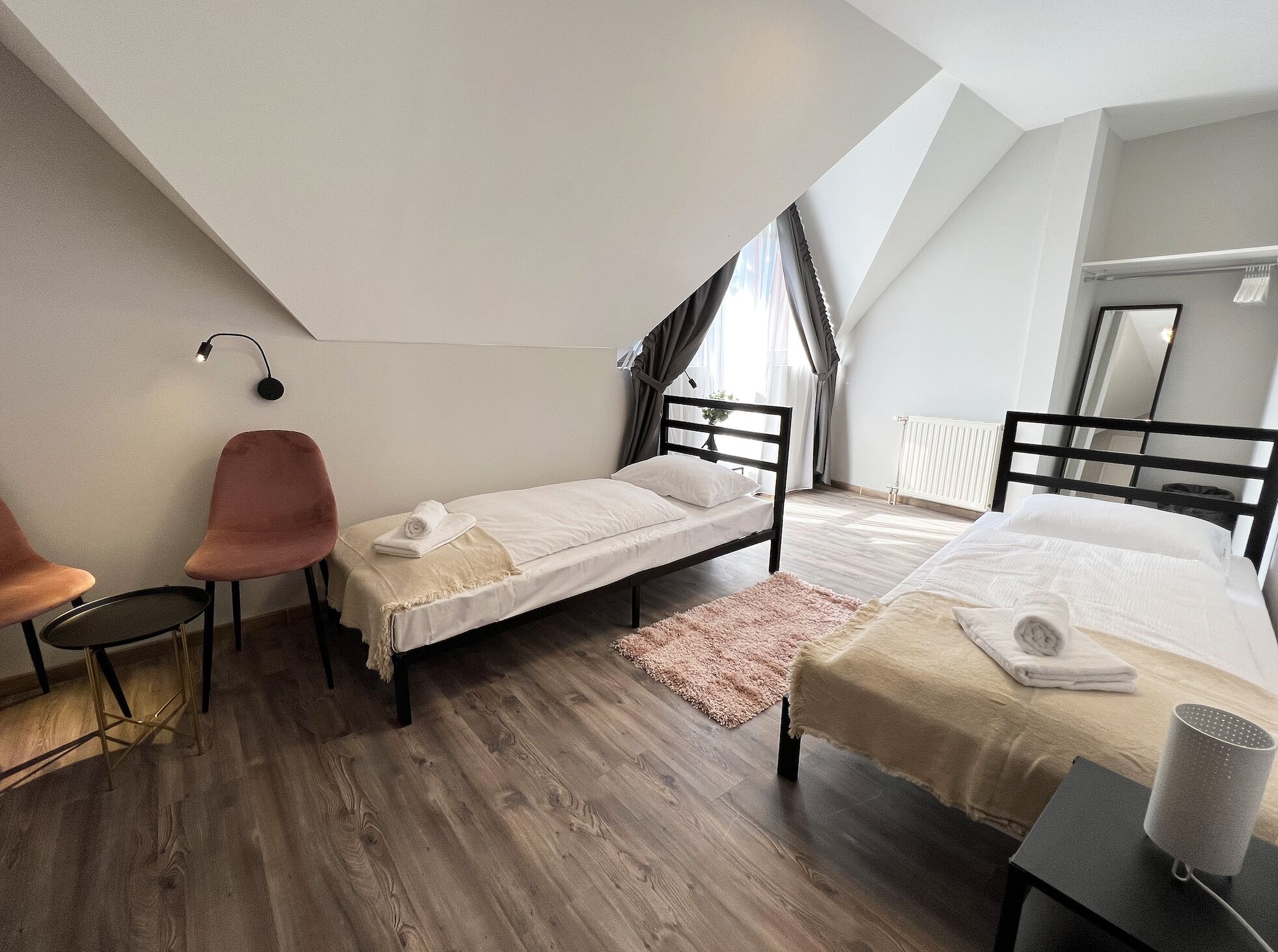 A modern bedroom with two single beds, a chair, a small table, and a radiator.