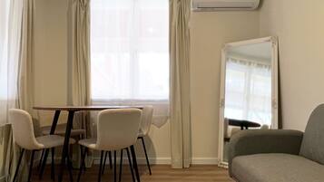 Een kamer met een eettafel en stoelen, een bank, een airconditioning en een spiegel.
