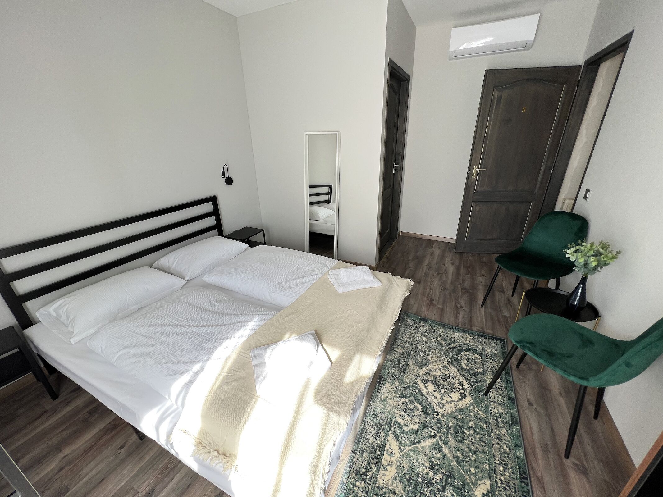 Una cama bien tendida con sábanas blancas, una silla verde y una mesita con un florero.