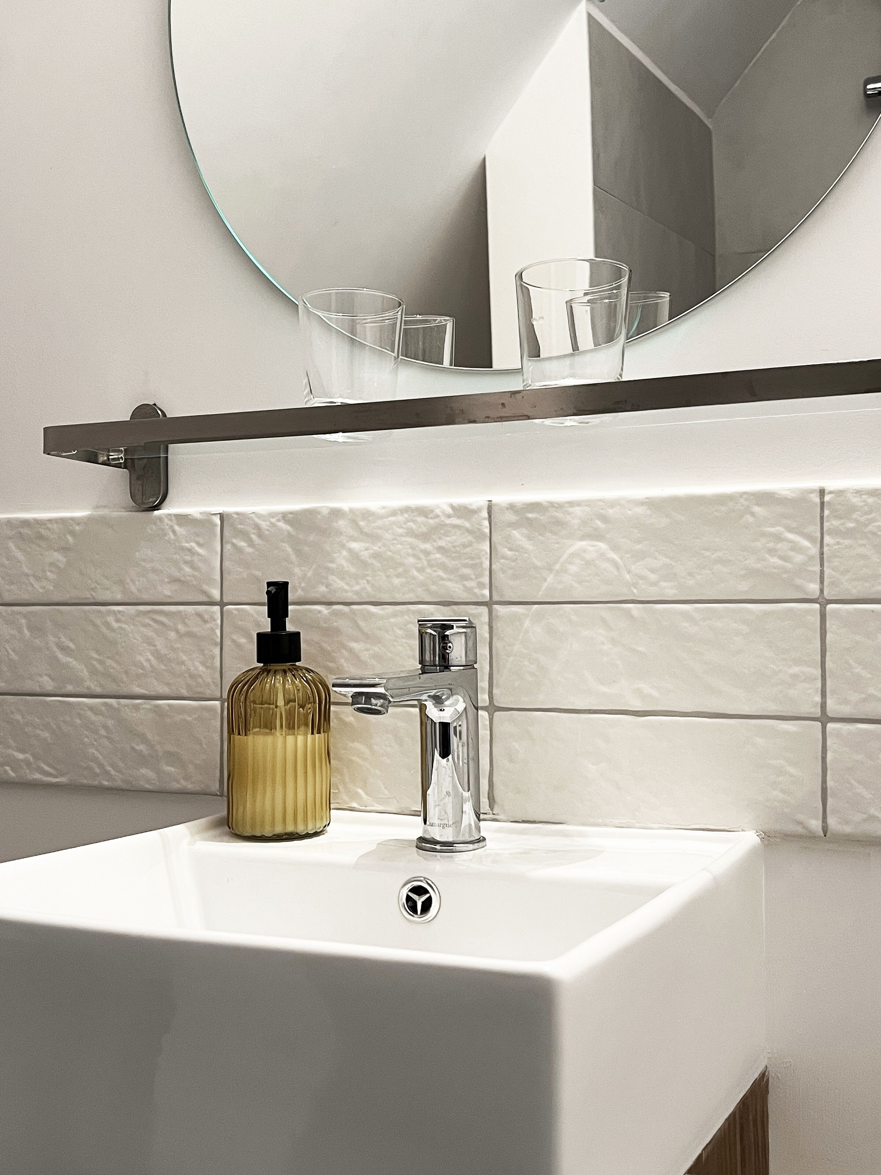 Ein Badezimmer mit einem weißen Waschbecken, einem Chrom-Wasserhahn, einem Seifenspender und einem Spiegel über dem Waschbecken.