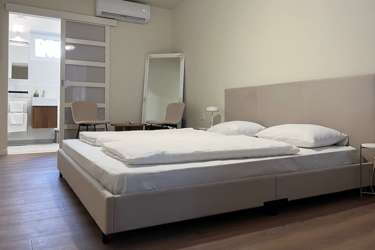 Une chambre moderne avec un grand lit, une table de chevet, une chaise, un miroir et un appareil de climatisation.