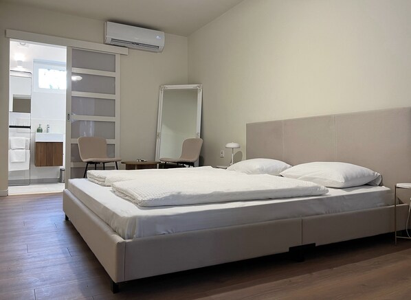 Un dormitorio moderno con una cama grande, una mesita de noche, una silla, un espejo y un equipo de aire acondicionado.