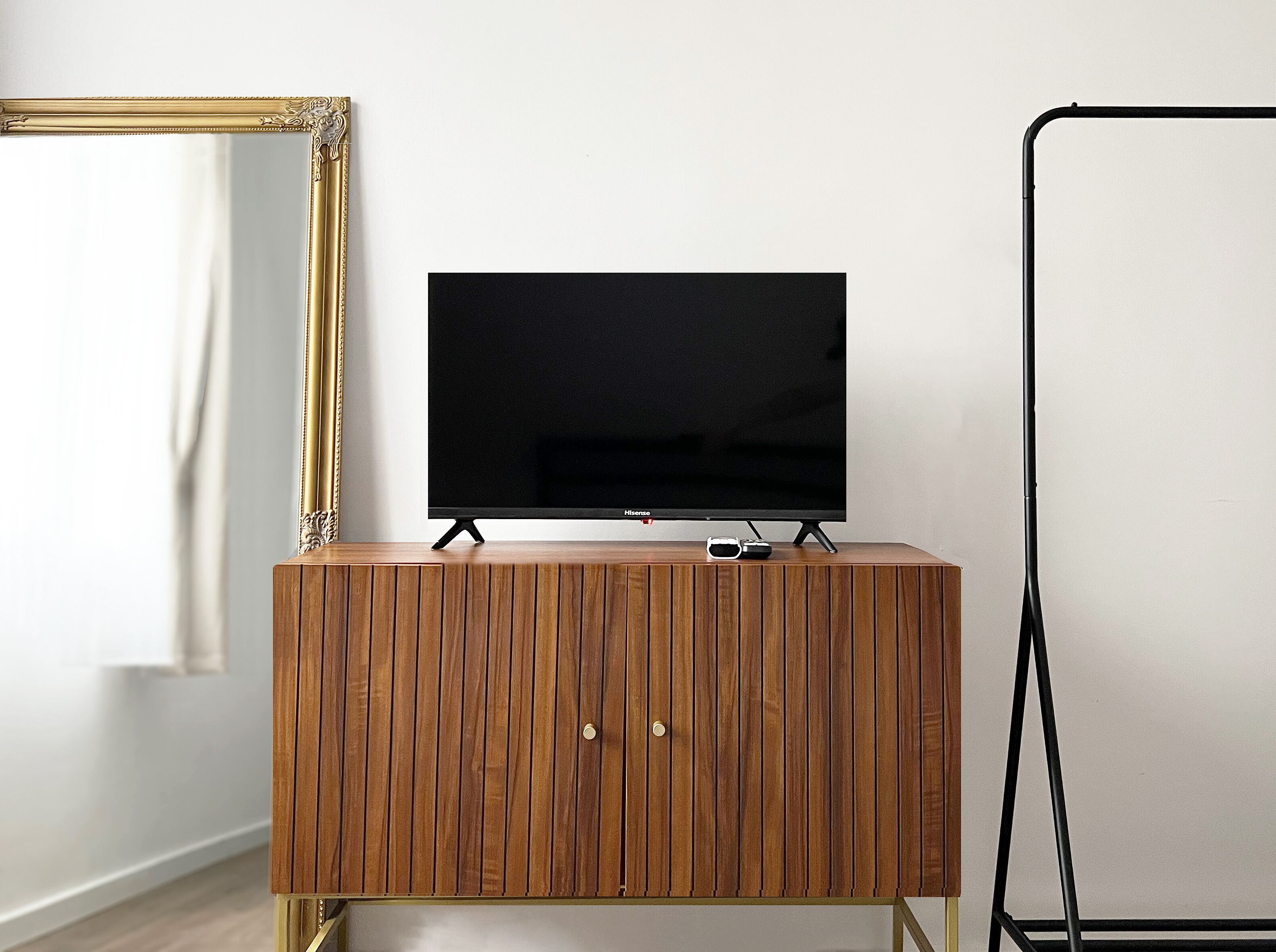 A wooden cabinet with a flat-screen TV on top, a gold-framed mirror, and a black tripod stand.