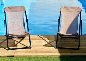 Deux fauteuils en osier, dotés d’une structure en métal et d’un dossier en treillis, sont placés sur une terrasse en bois, près d’une piscine.