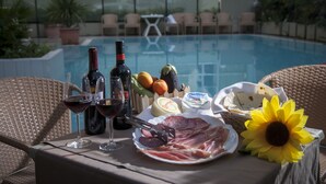 A table with food and drinks by a poolside, including a plate of meats, cheese, and a sunflower. - Si Rimini Hotel (Rimini)