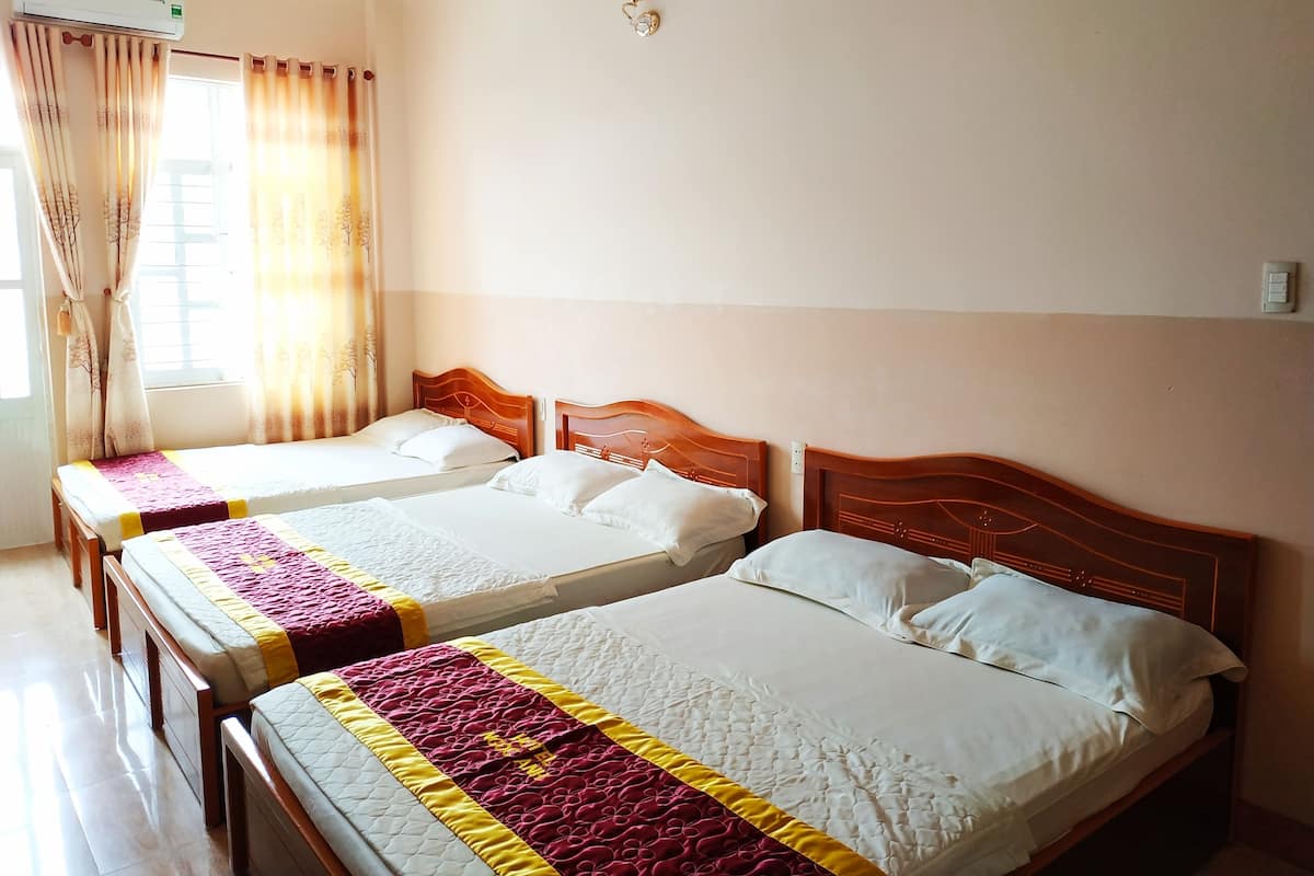 A hotel room with two beds, a window with curtains, an air conditioning unit, and a wall-mounted light fixture.
