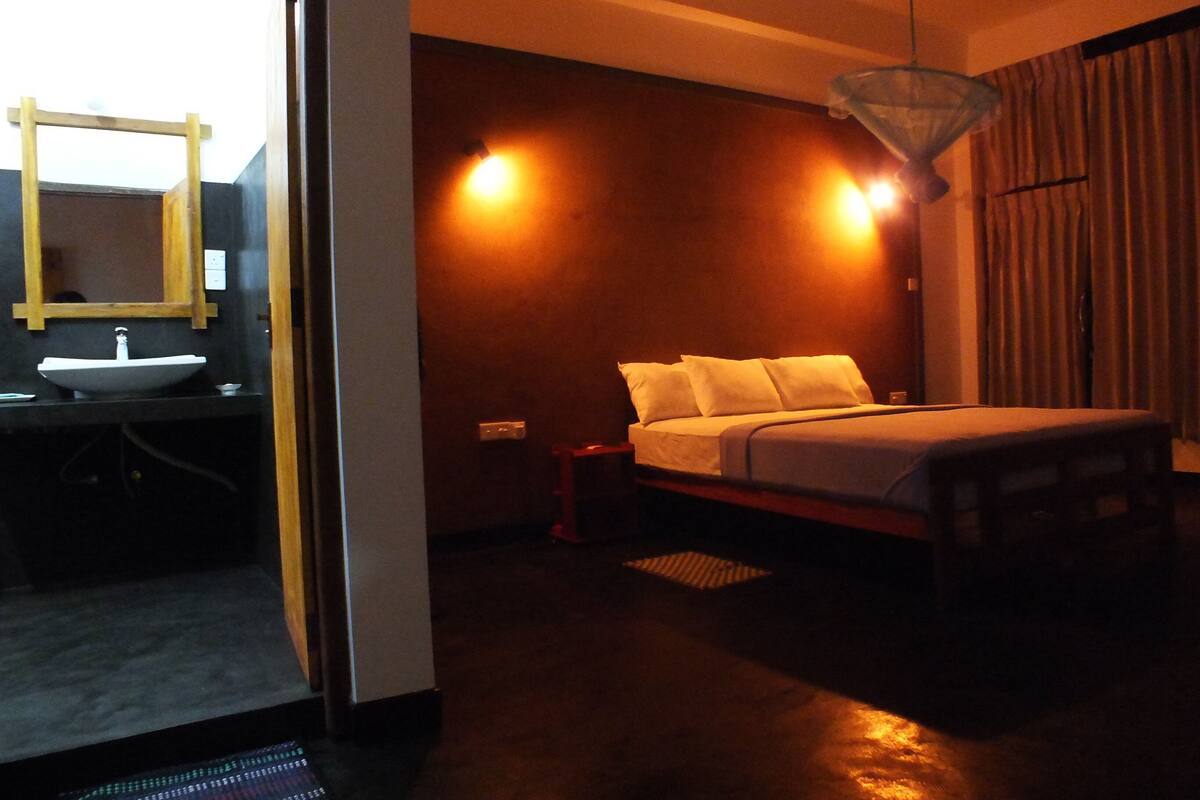 A bedroom with a bed, bedside table, and a mirror above the sink.