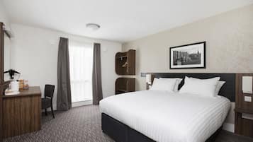 A hotel room with a large bed, a desk with a chair, a coat rack, and a framed picture on the wall.
