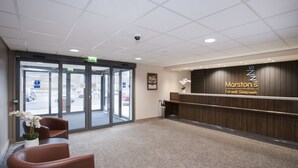 A hotel reception area with a reception desk, seating area, and a view of the parking lot. - Spring River Ebbsfleet by Marston's Inns (Gravesend)