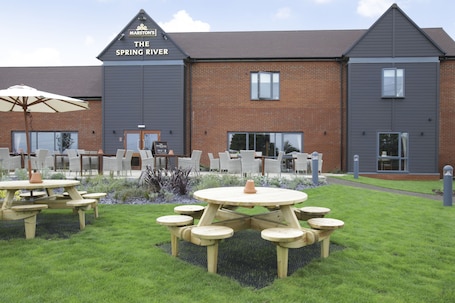 A building named 'The Spring River' with a brick facade, multiple windows, and outdoor seating with tables and chairs.