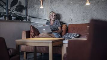 Una persona sentada en un sofá de cuero con una computadora portátil, en una habitación con pared de concreto y lámparas colgantes.
