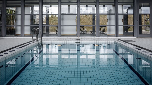 A swimming pool with clear blue tiles, metal ladders, and a view through large windows to the outside. - Fårösunds Fästning (Fårösund)