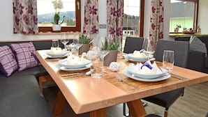 Un'area pranzo con un tavolo in legno apparecchiato per quattro persone, circondata da divani grigi e cuscini viola.