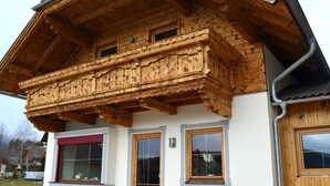 Un edificio in stile chalet con un balcone in legno, ampie finestre e una facciata bianca.