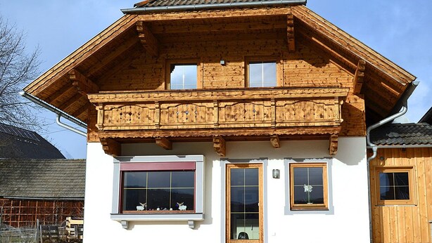 Una baita in legno con un balcone, ampie finestre e una porta.