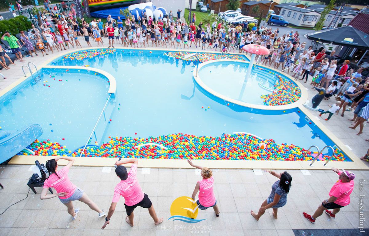 Uma piscina cercada por um grupo de pessoas, com uma piscina de bolinhas cheia de bolas coloridas.