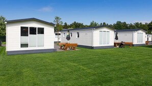 Una hilera de casas móviles con césped, bancos de madera y mesas de picnic.