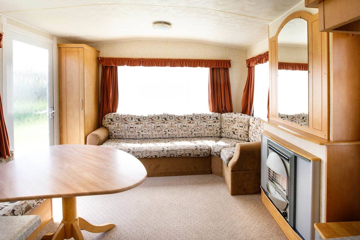 Un intérieur de camping-car compact comprenant un canapé, une table à manger, une cheminée et une grande fenêtre avec des rideaux.