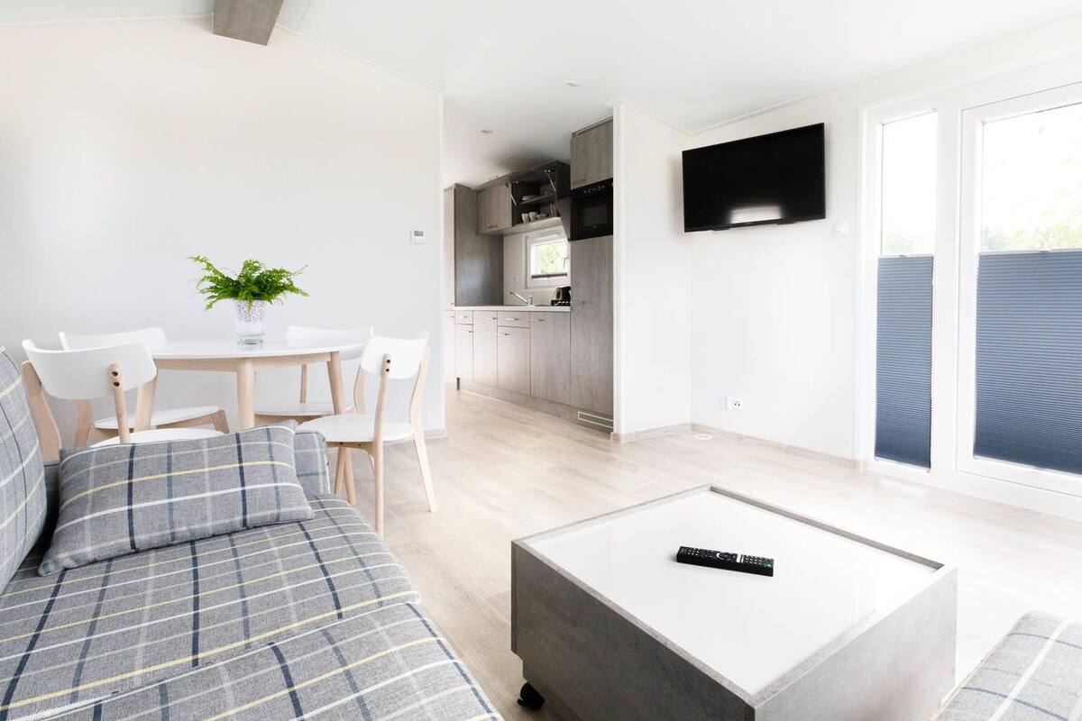 Un salon moderne avec un canapé, une table basse et un coin repas comprenant des chaises et une table. On aperçoit une cuisine au fond.