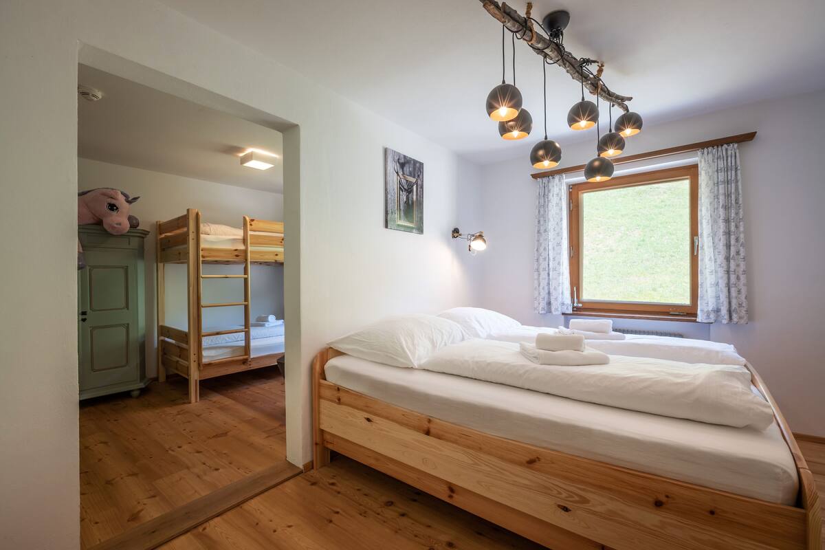 Un dormitorio con una cama litera de madera, una cama individual, una ventana con cortinas y una lámpara colgante.
