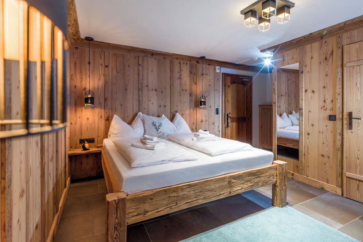 Una cama con estructura de madera, ropa de cama y almohadas blancas, una mesita de noche con lámpara y un armario de madera.