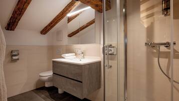 Un baño con diseño moderno, que incluye una cabina de ducha de vidrio, un lavamanos blanco y un inodoro.