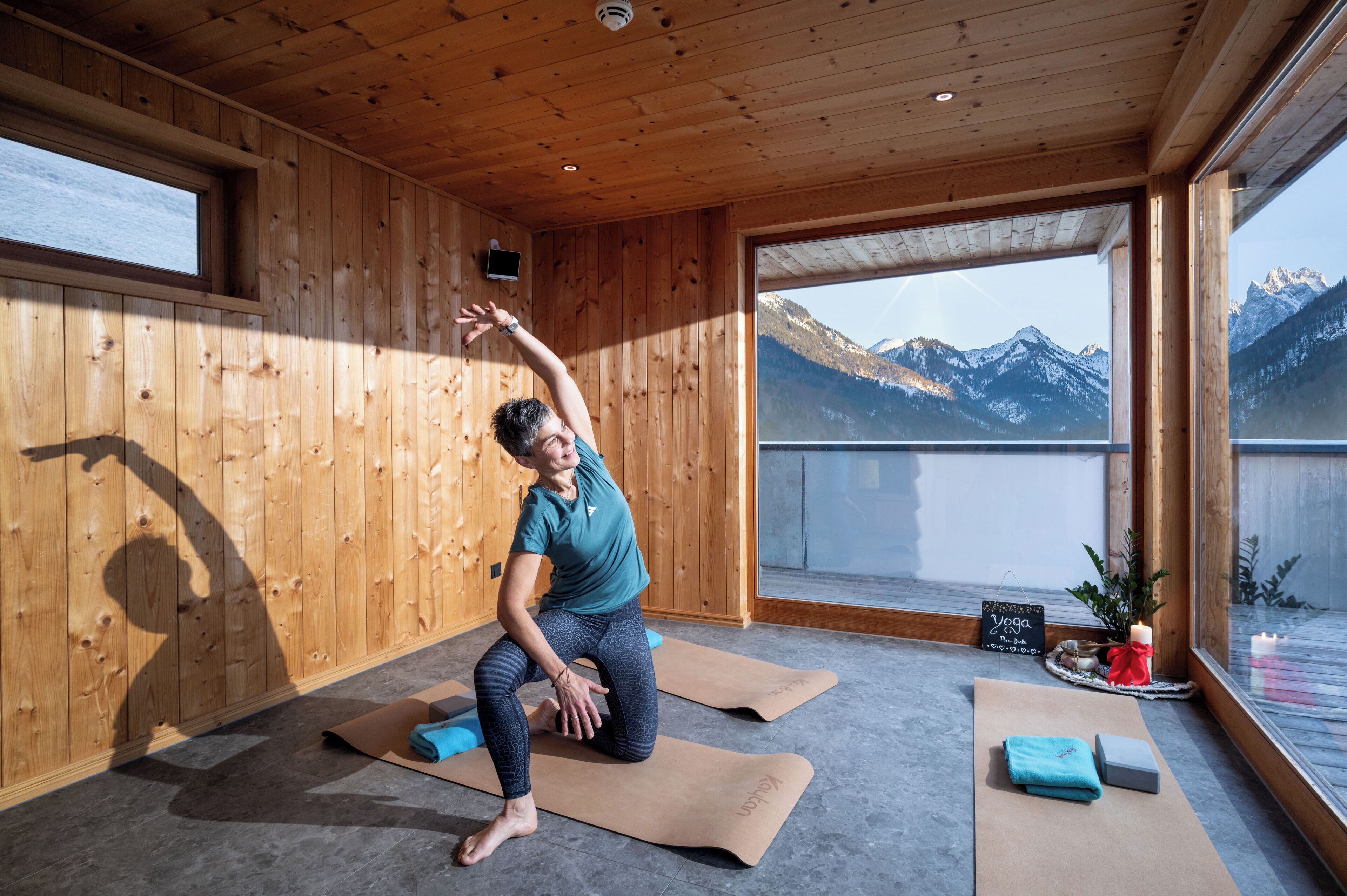A yoga room with wooden walls, large windows, and a view of mountains.