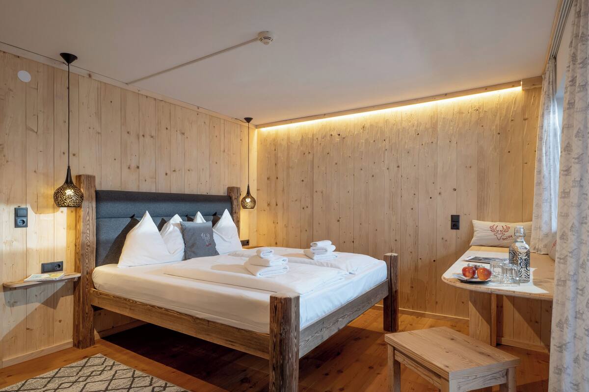 Habitación con paneles de madera, una cama, una mesita de noche y una pequeña mesa con una botella y vasos.