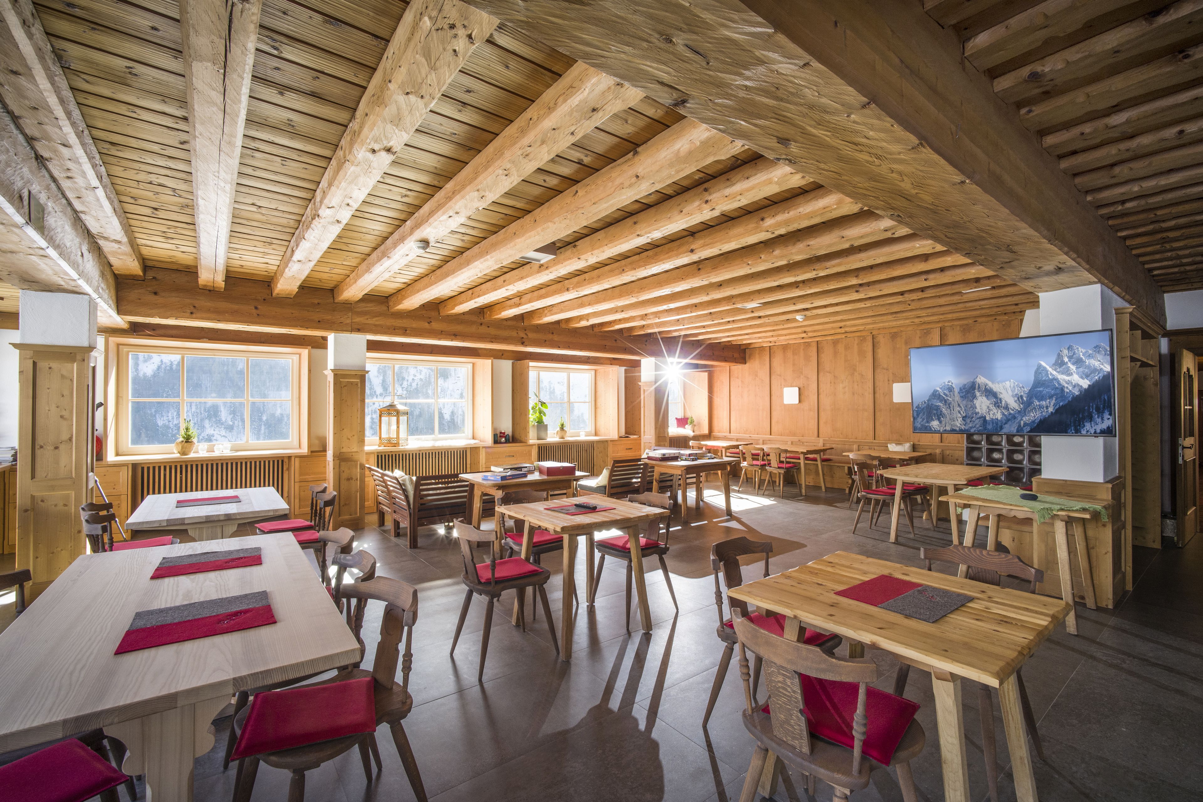 A spacious dining area with wooden tables and chairs, large windows with mountain views, and a television on the wall.