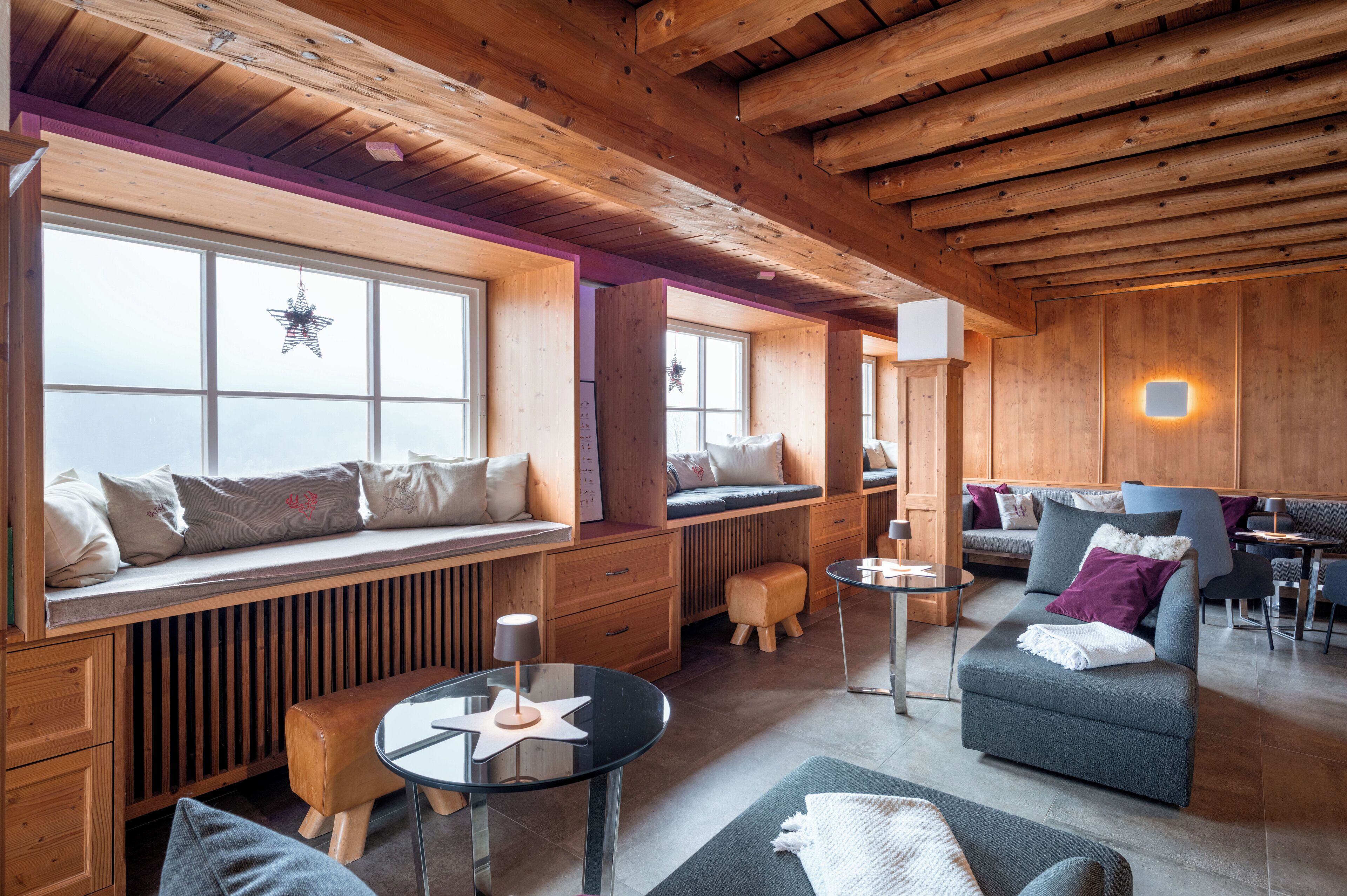 Een gezellig cabin-interieur met houten balken, een zithoek met kussens, een kleine tafel en een bank.